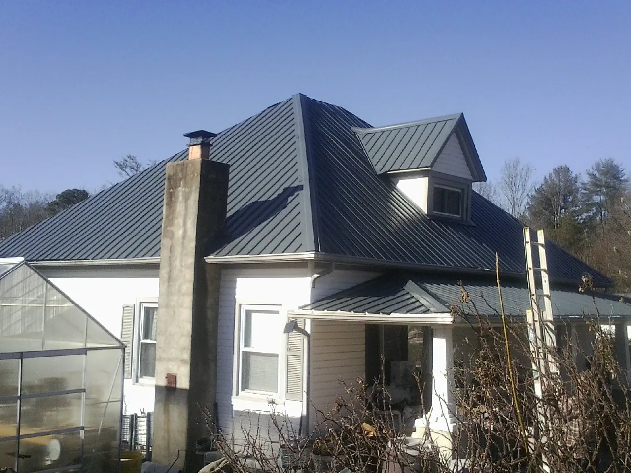 Dark blue standing seam metal roof on a white farmhouse with dormer — Slate & Tile Roof Repair by Roofing Brothers in New Goshen