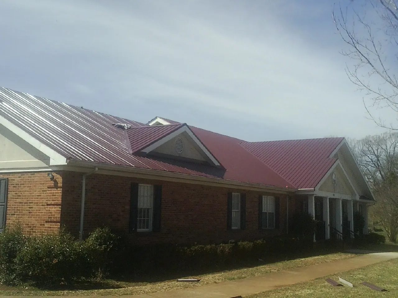 Red metal roof with gabled entries on a long brick building, from a Hail Damage Roof Repair job in New Goshen