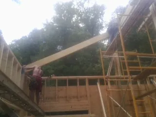 Carpenter raising a rafter beam on a new second story frame in New Goshen