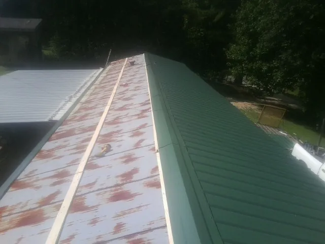 Old rusted panels beside newly installed green metal roofing — Wind Damage Roof Repair by Roofing Brothers in New Goshen