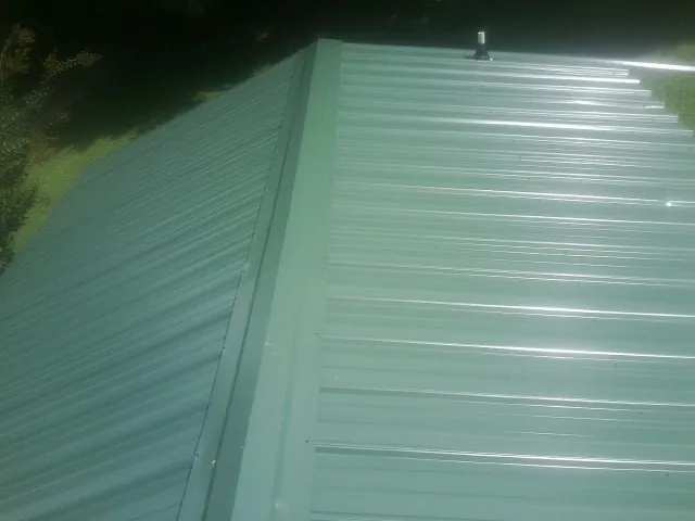 New green metal panels meeting at the ridge of a roof — Flat Roof Repair work by our crew in New Goshen