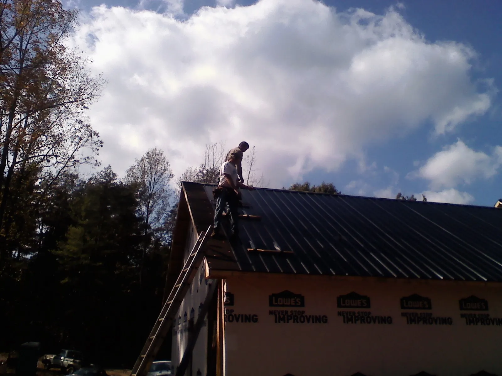 Roofer fastening dark metal panels high against a cloudy sky, from a Roof Inspection job in New Goshen
