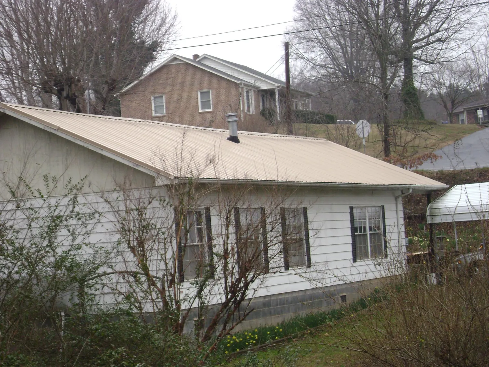 Tan metal roof on a white sided house set into a hillside — Commercial Roofing by Roofing Brothers in New Goshen